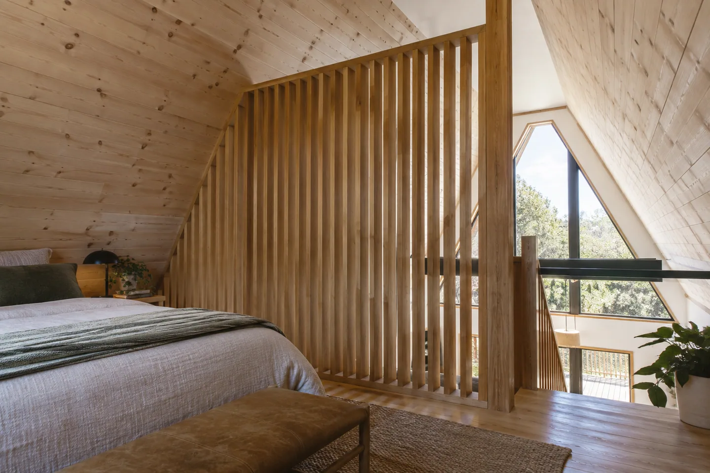 A slatted timber privacy divider at the edge of an A-frame loft, open light above it