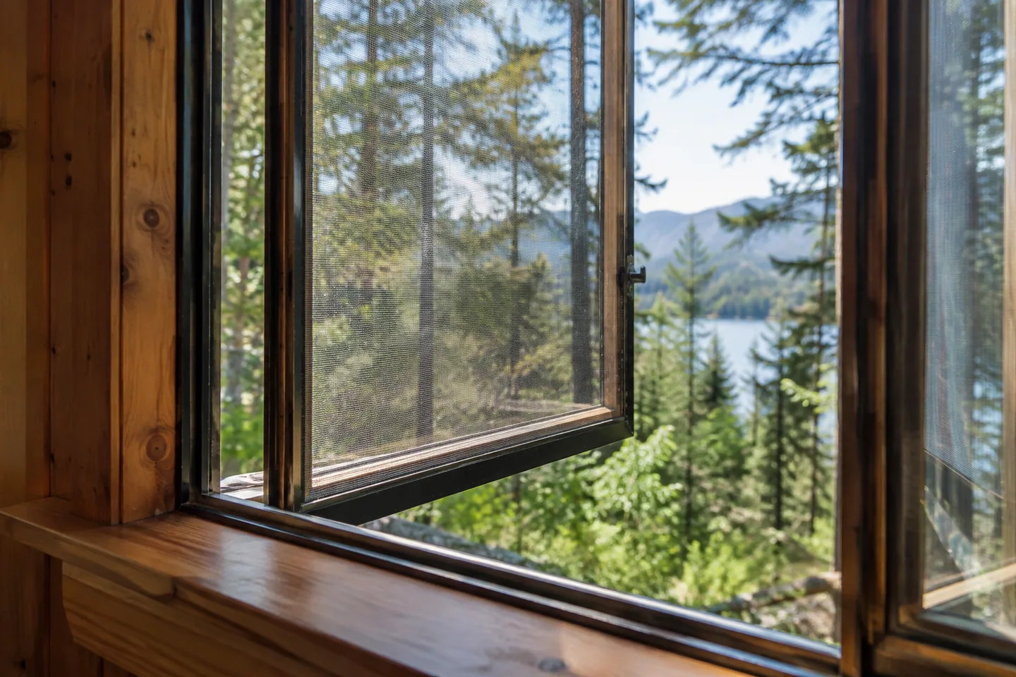 Macro view of an open cabin casement window with fine insect mesh screen and forest beyond